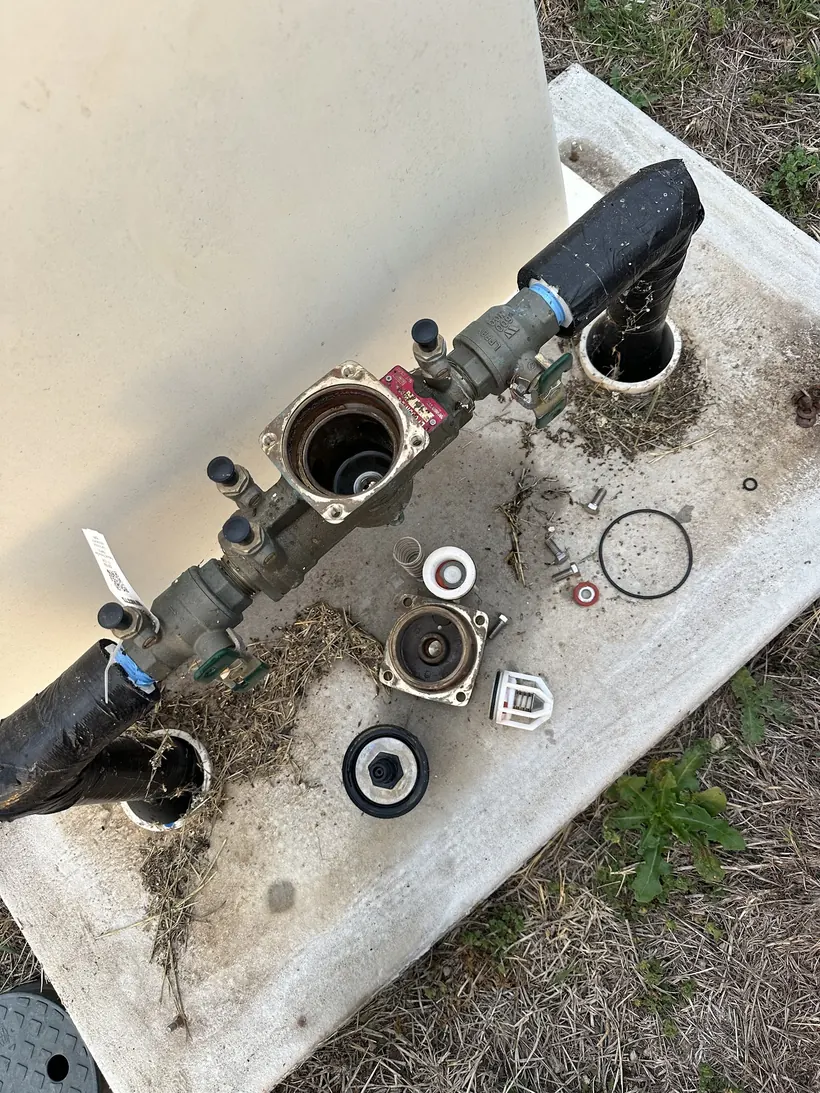 An opened backflow preventer on a concrete pad at Cove Plumbing, internals laid out for testing